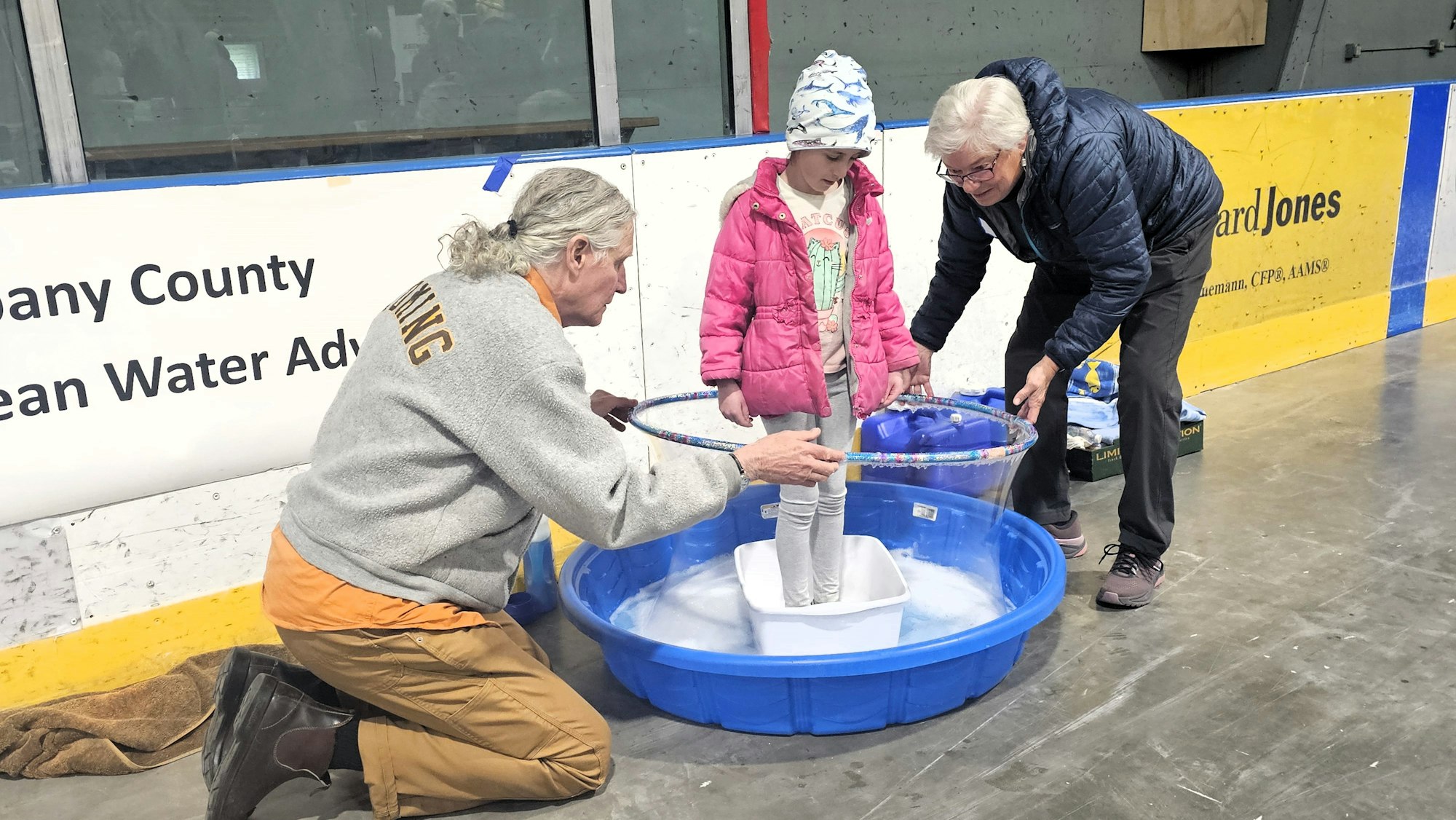 Two adults show a child a water science experiment in an indoor setting.