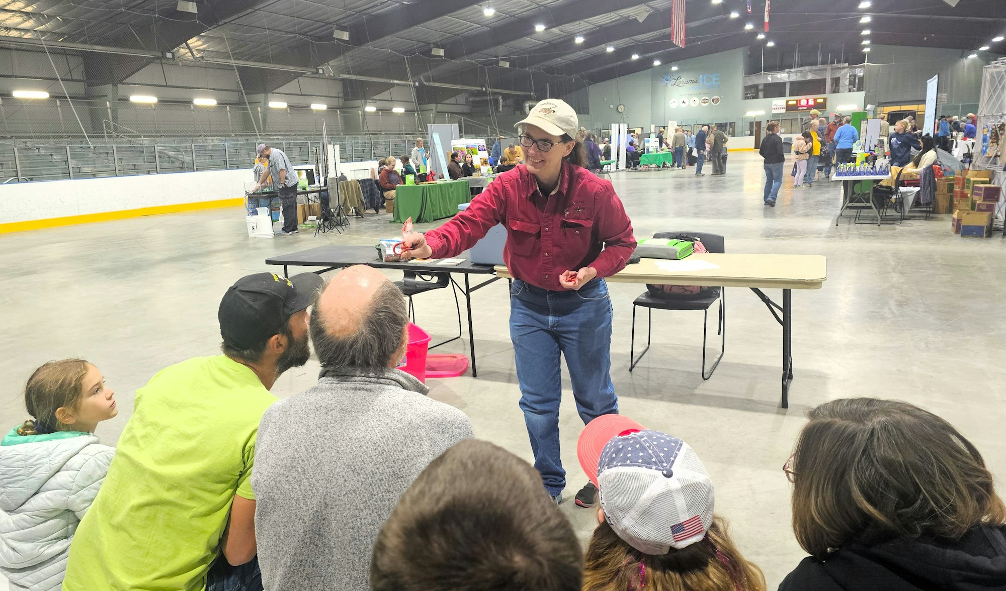 Indoor event with people, a person in red shirt handing out papers to attendees, booths in background.
