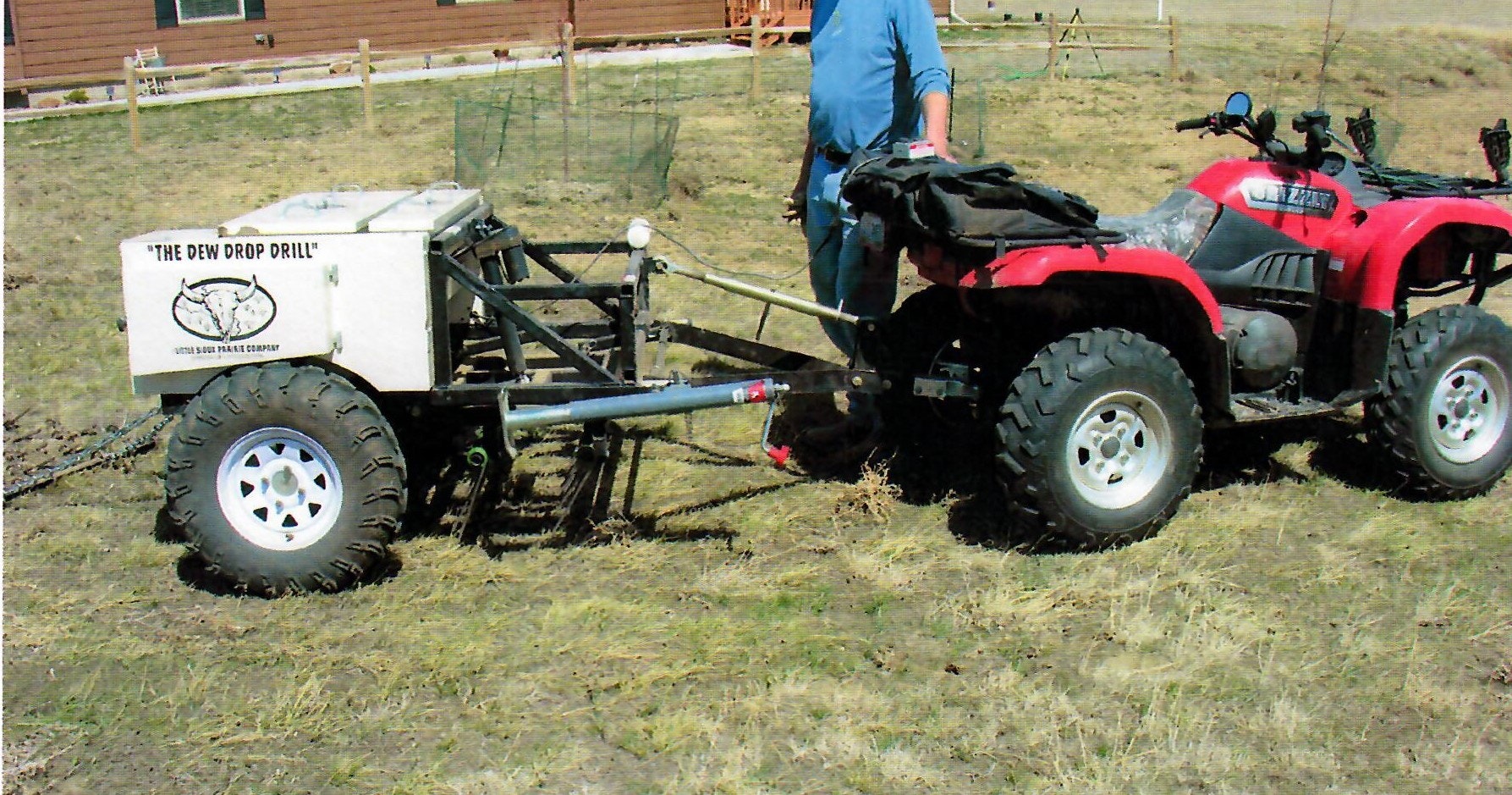 An ATV attached to a piece of agricultural equipment called "The Dew Drop Drill" for planting seeds, with a person operating it outdoors.