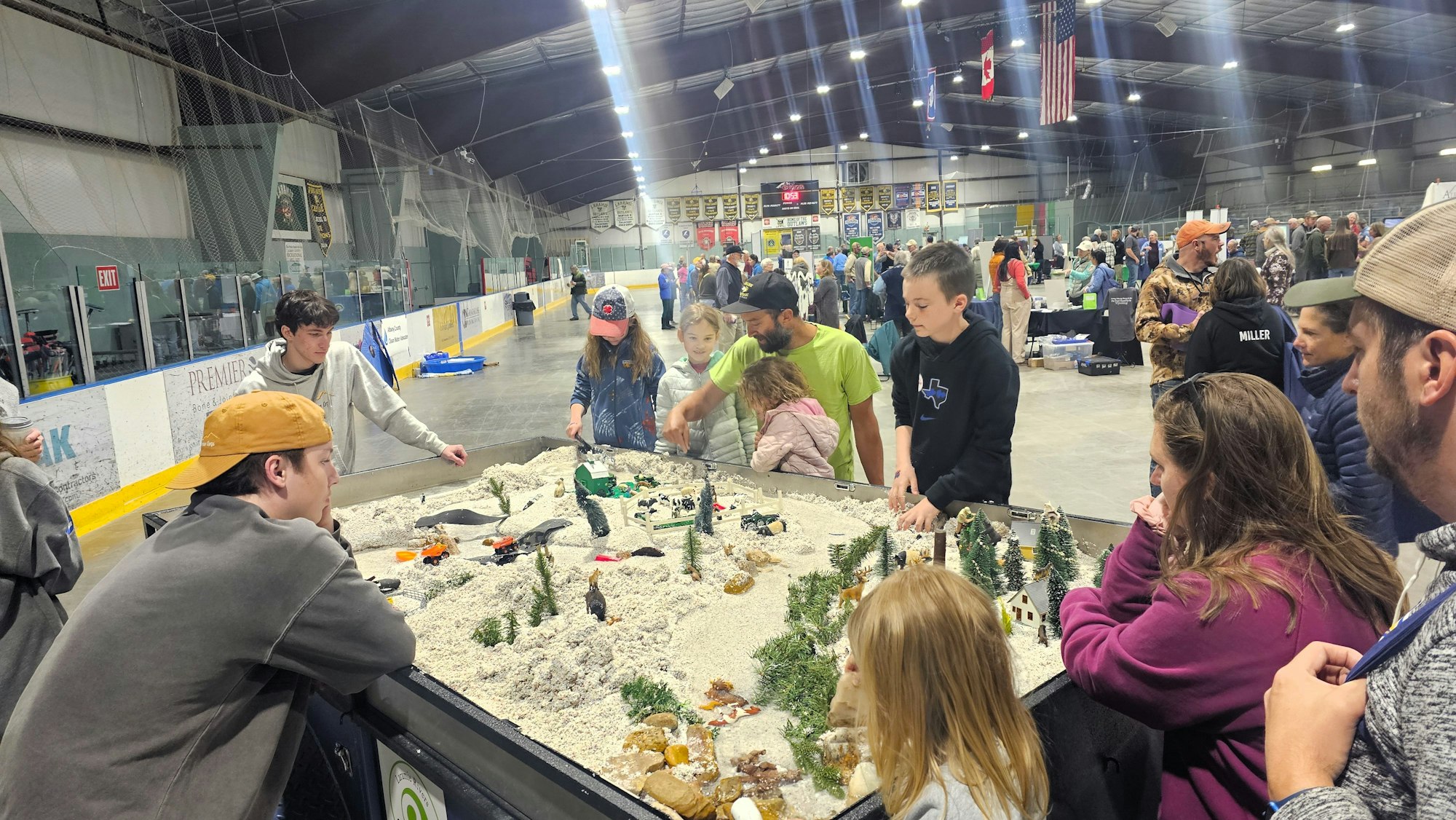 People gathered around a miniature display at an indoor venue, observing and interacting with the setup.