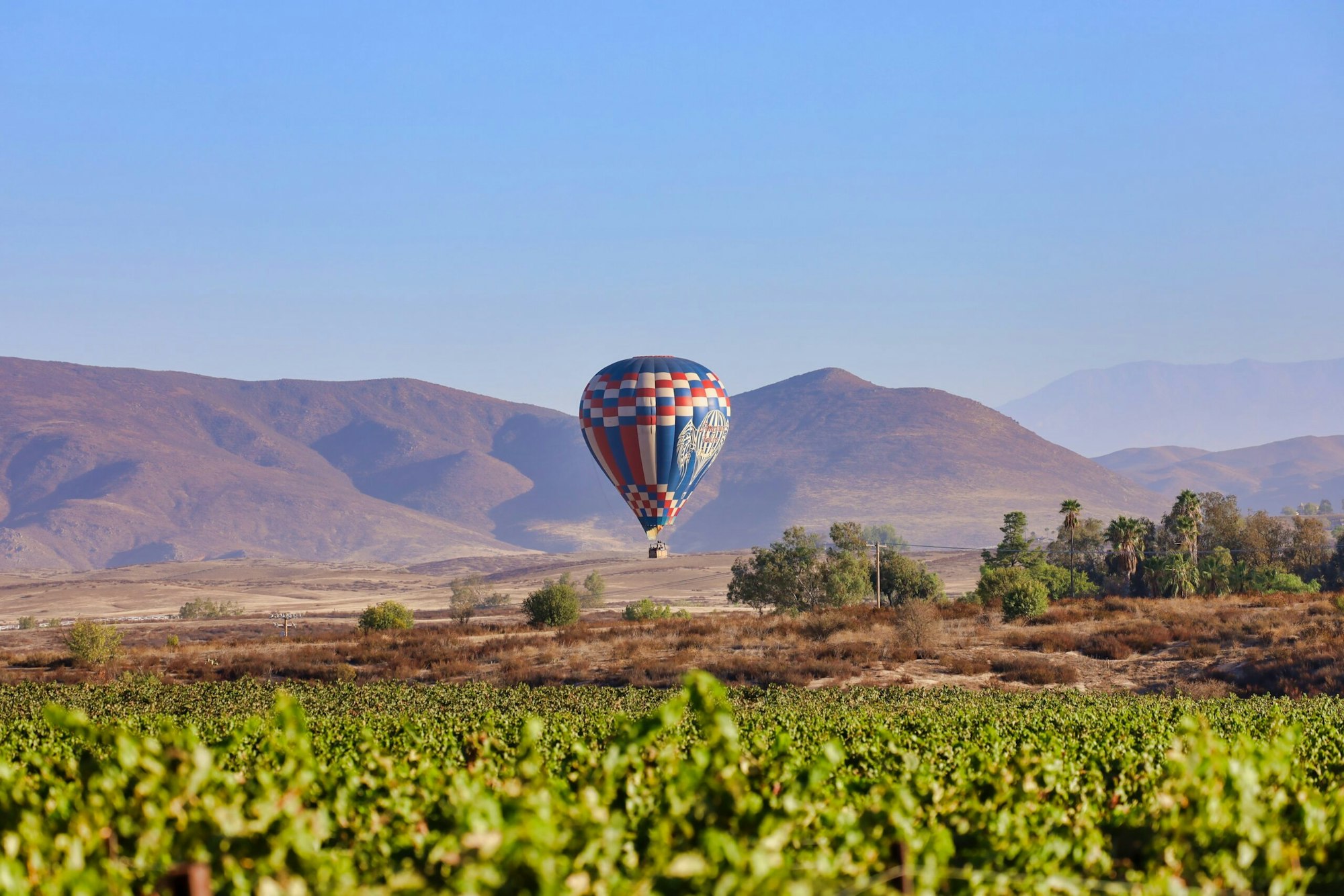A hot air balloon flies over a scenic landscape with mountains and greenery.