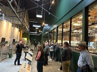 A group of people on a tour inside a brewery, observing equipment behind glass walls.