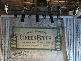 A wall-mounted advertisement for Nelson's Green Brier Tennessee Whiskey with row of liquor dispensers above it.