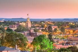 A cityscape at sunset with buildings, greenery, and a clear sky.