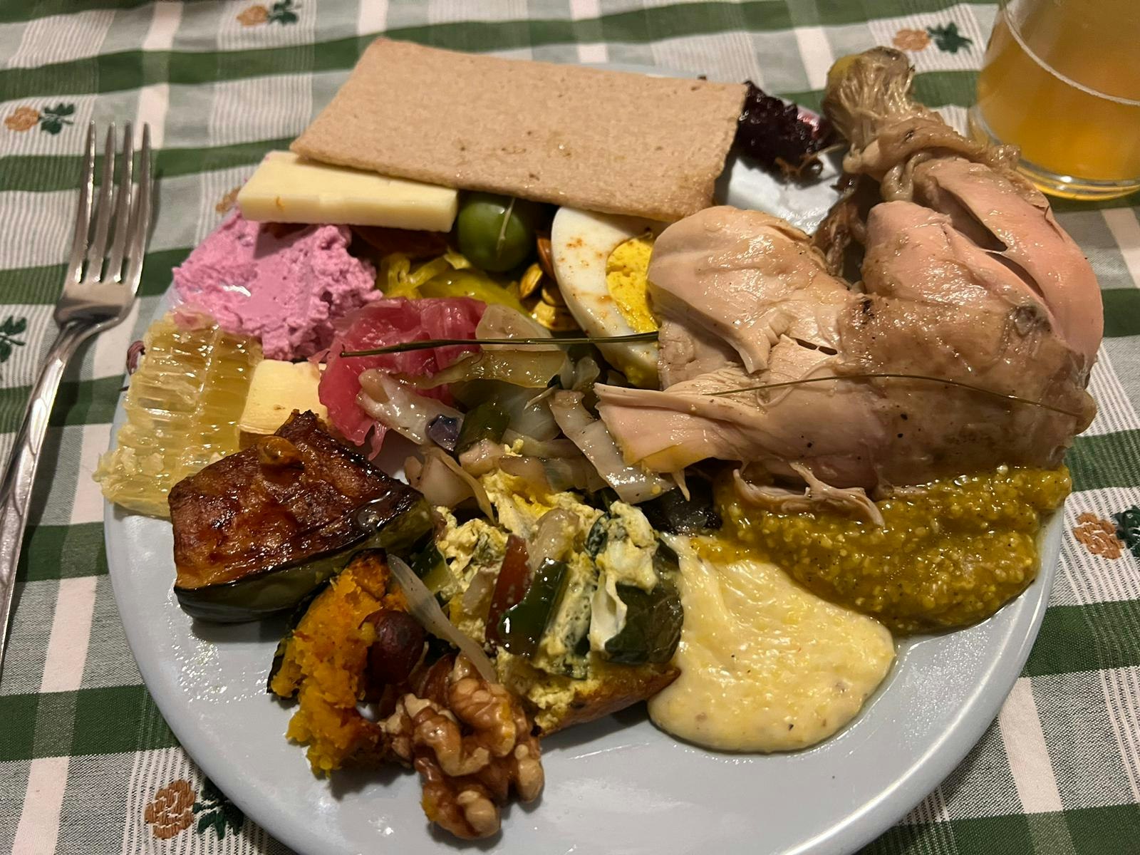 A plate with a variety of foods including meat, sauce, cheese, crackers, salad, and a piece of honeycomb on a checkered tablecloth.