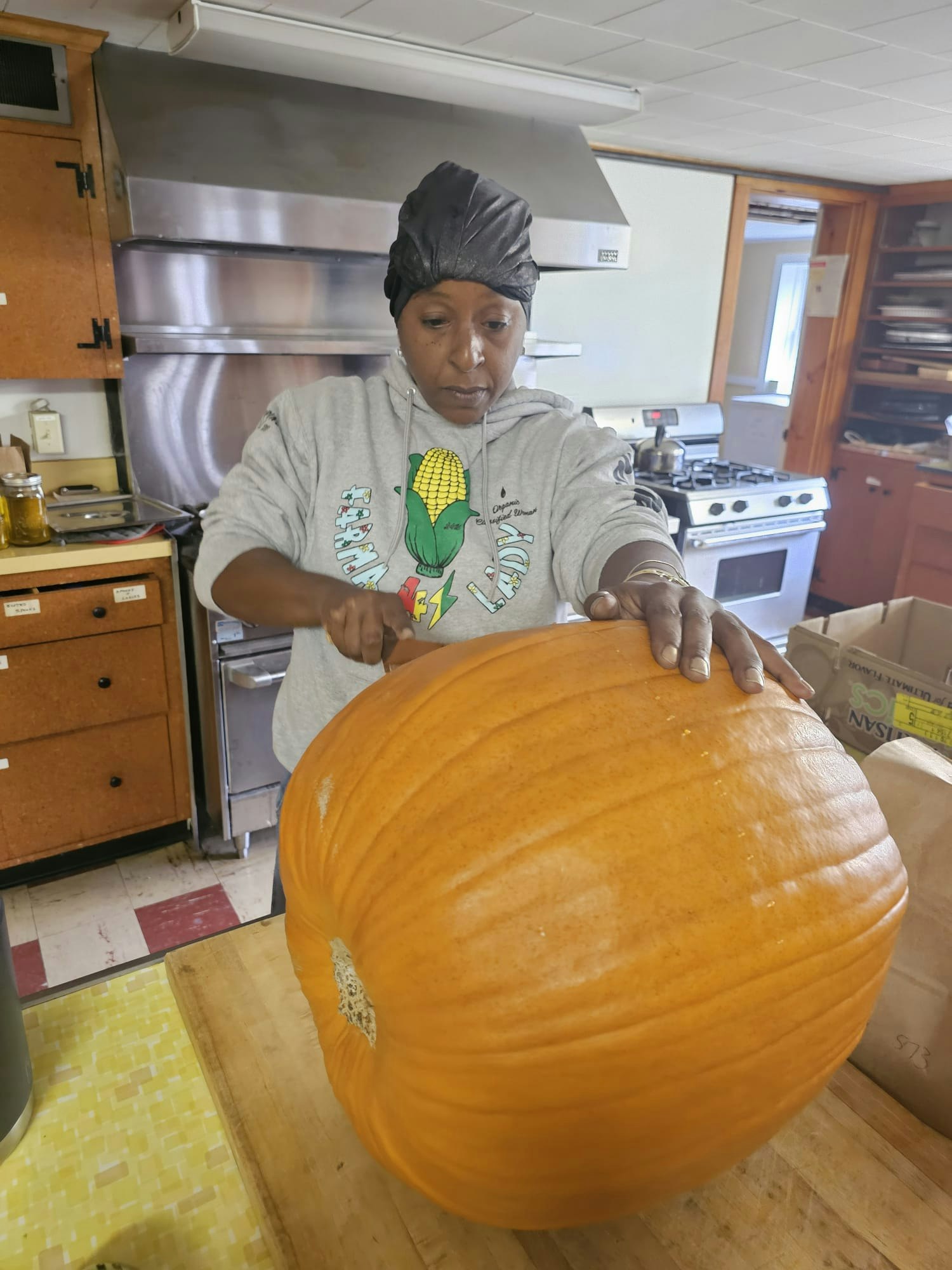 Person in a kitchen cutting a large pumpkin on a wooden table.