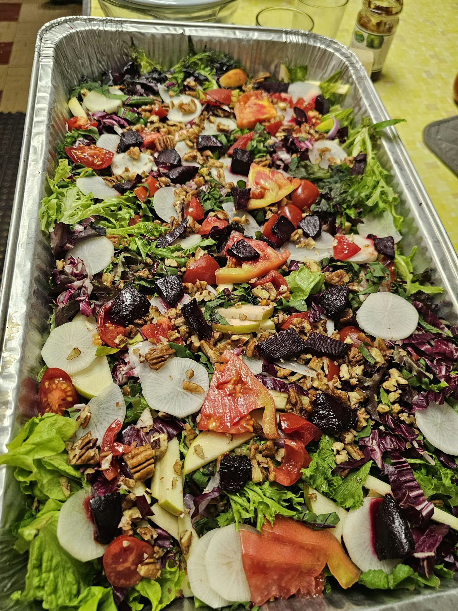 A colorful salad in a tray with mixed greens, radishes, tomatoes, beets, and nuts.