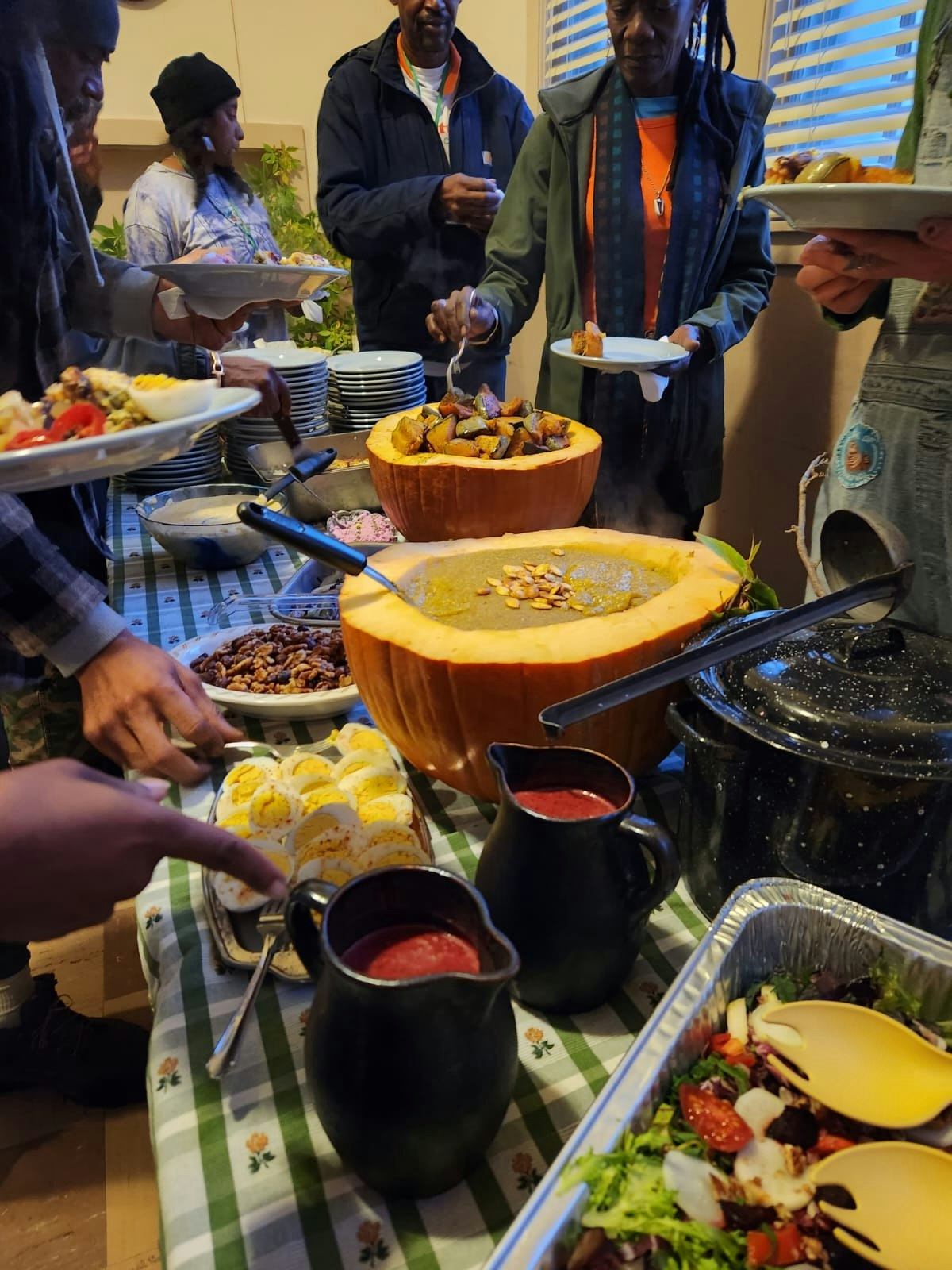 Buffet with sliced eggs, salads, soup in pumpkin bowls, and people serving themselves.