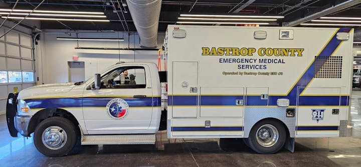 It’s a Bastrop County Emergency Medical Services truck parked indoors, featuring medical service graphics and 911 signage.