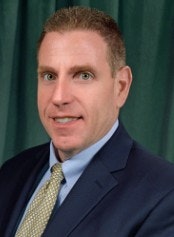 A person in a suit and tie is posing against a greenish background.
