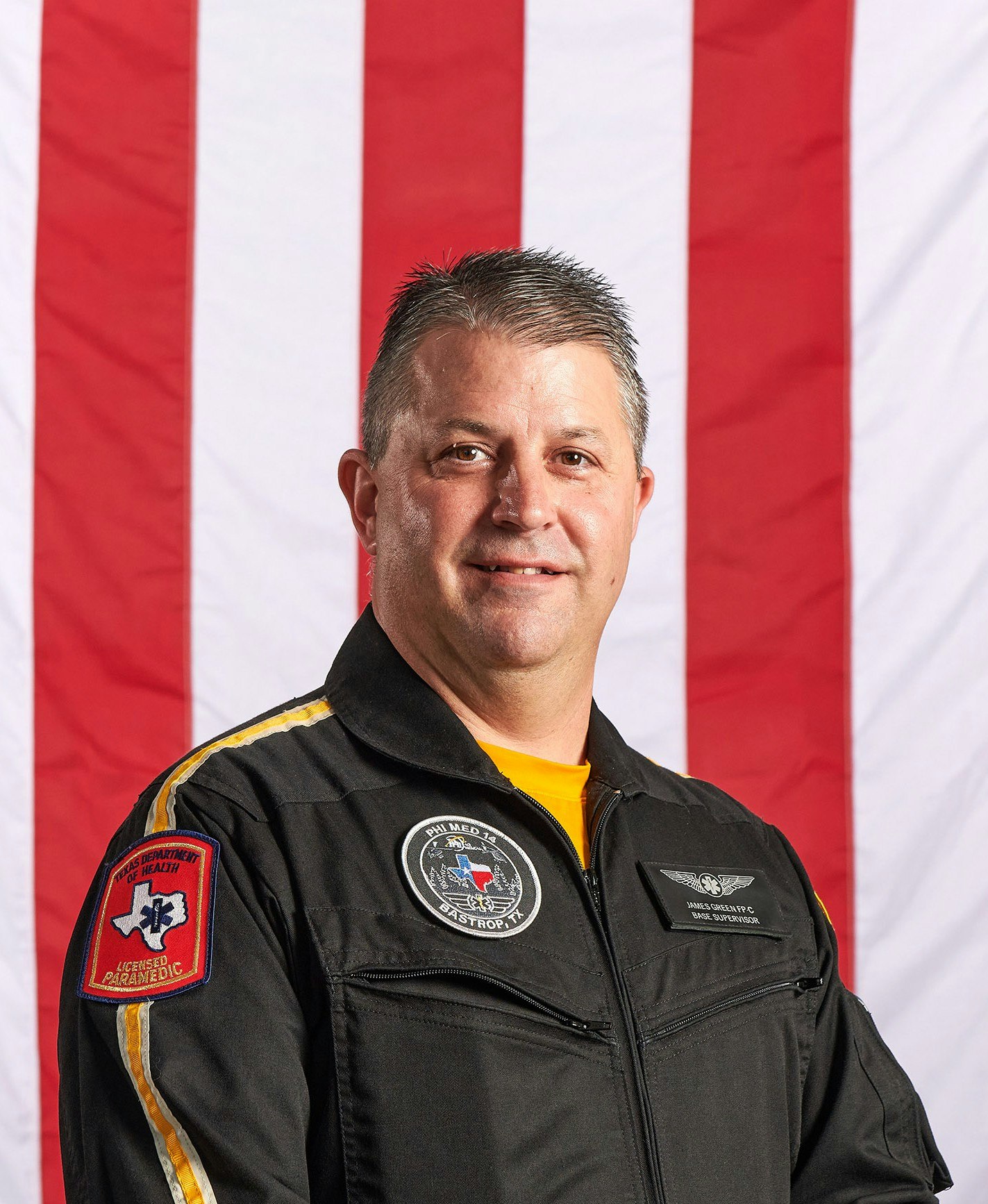 A person in a uniform stands in front of an American flag. The uniform has a "Licensed Paramedic" patch.