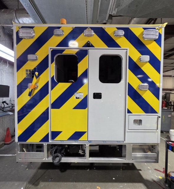 The image shows the back of a vehicle with a bright yellow and blue diagonal striped design, featuring doors and various lights.