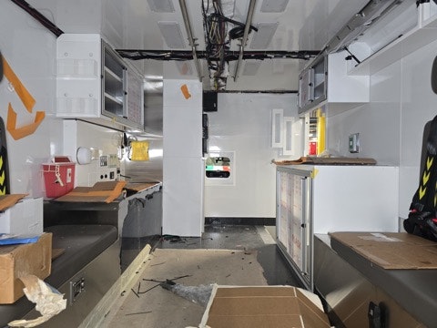 The image shows the interior of a vehicle, likely an ambulance or medical unit, with empty cabinets and some scattered materials.