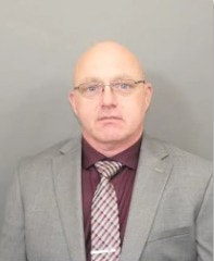 A person wearing glasses, a gray suit, and a striped tie against a plain background.