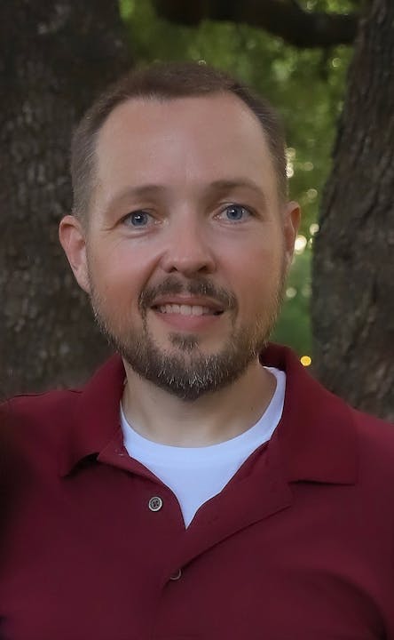 The image features a man smiling outdoors, wearing a dark red polo shirt, with trees in the background.