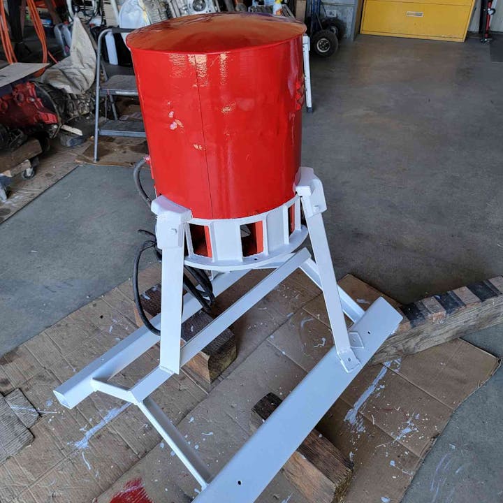 A red cylindrical object with a white metal frame in a workshop.