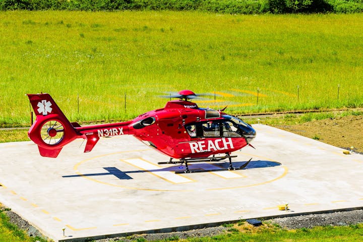 Red emergency helicopter on a helipad in a grassy area.
