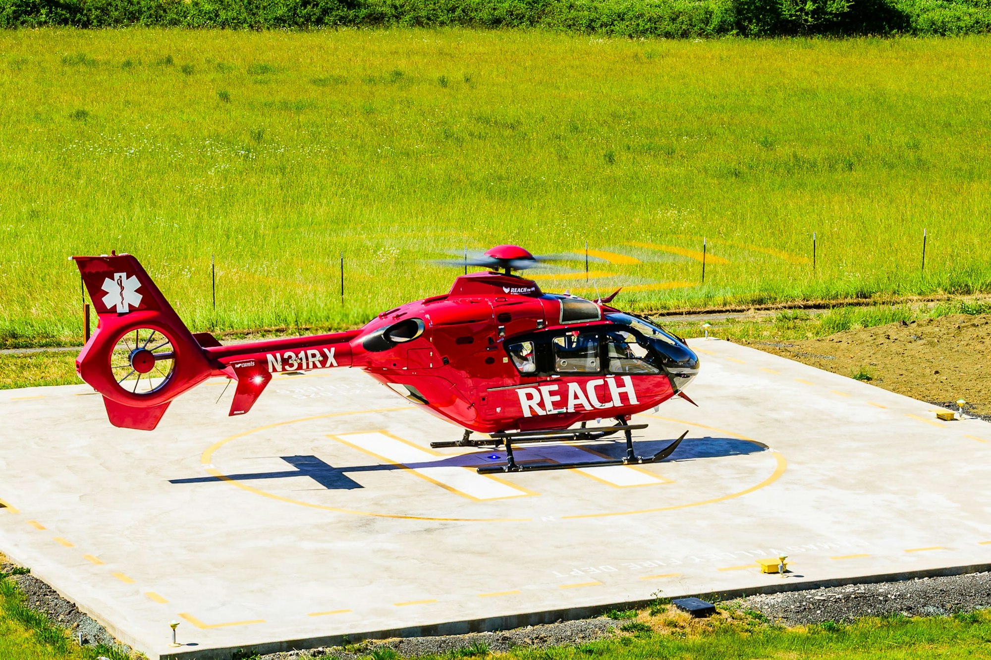 Red emergency helicopter on a helipad in a grassy area.