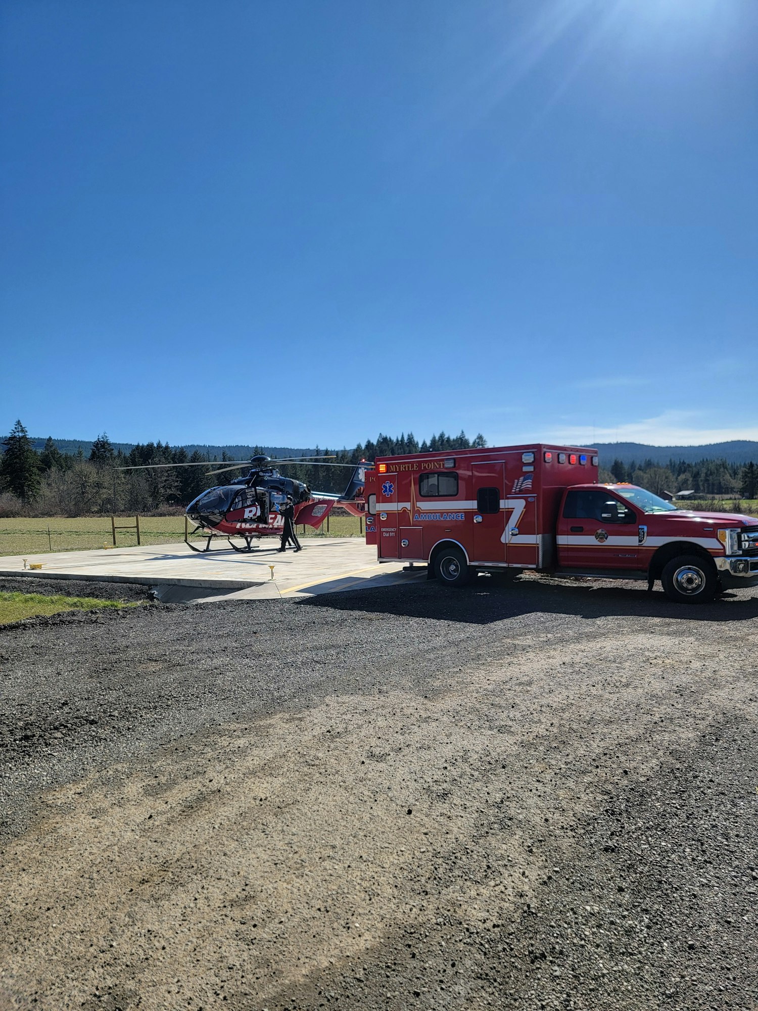 A red ambulance and a helicopter are parked near each other on a sunny day.