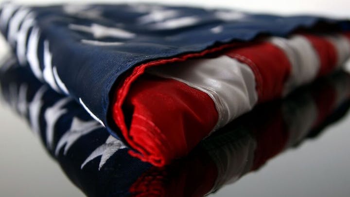 A folded American flag with stars and stripes, reflected on a surface.