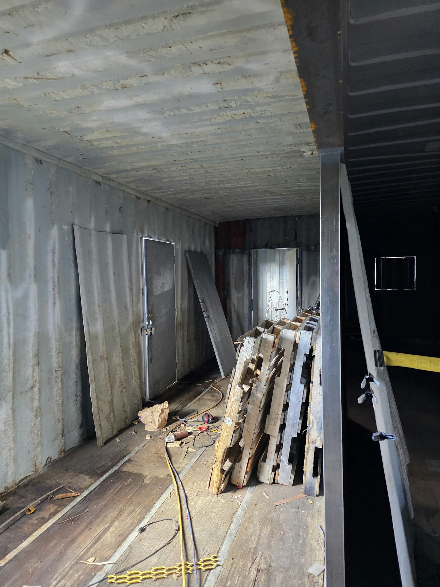 Interior of a metal container with scattered pallets, cables, and tools.
