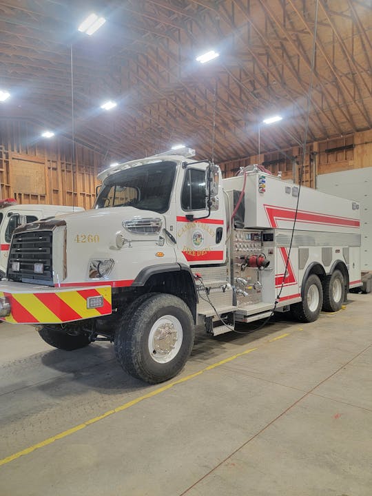 A fire truck inside a large garage or fire station with wooden rafters and bright lights.