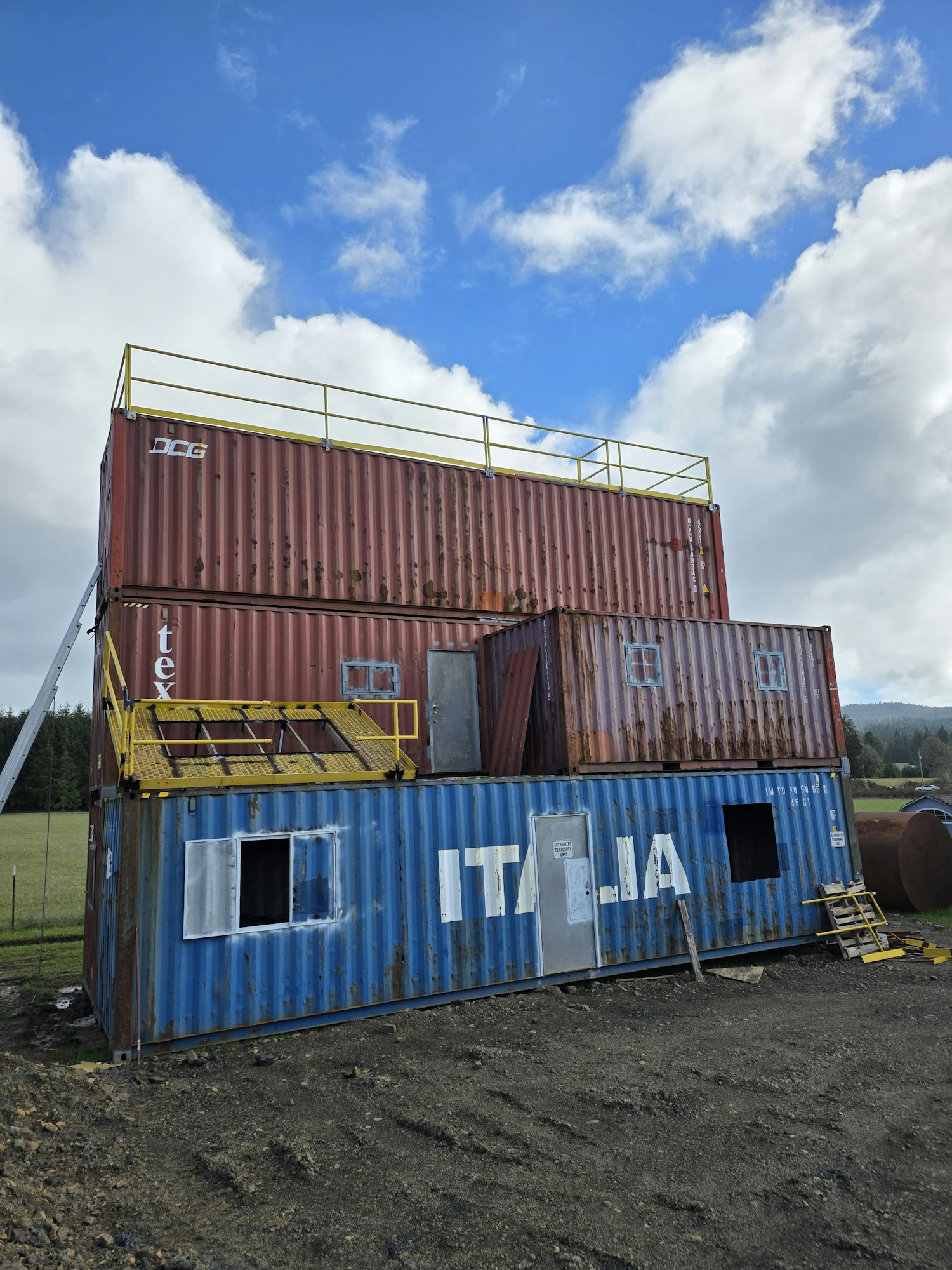 Stacked shipping containers with stairs and railings, under a partly cloudy sky.