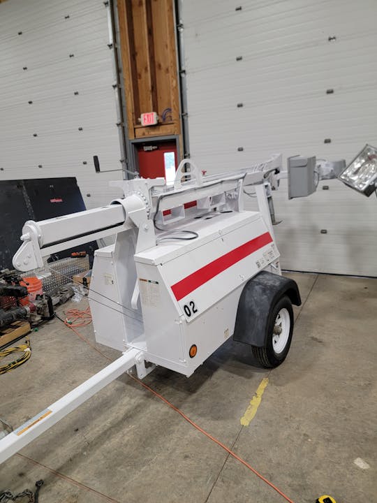 A portable light tower machine inside a garage with concrete floor and overhead door.