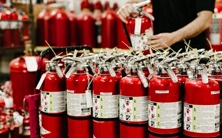 Rows of red fire extinguishers with labels are being inspected by a person.