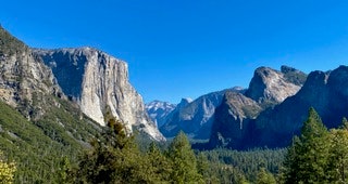 A scenic view of a mountainous landscape with cliffs, green forests, and a clear blue sky.