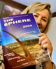 A person holding a magazine titled "THE SPHERE 2024."