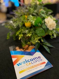 A welcome program for a CALAFCO awards banquet lies on a table next to a floral arrangement.
