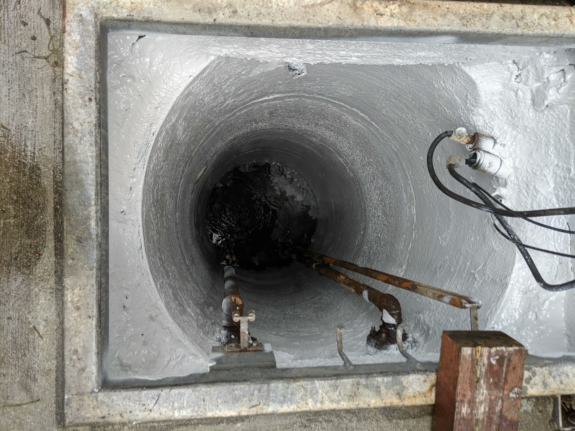 Concrete well opening with internal coating, pipes, wires, and slight corrosion.