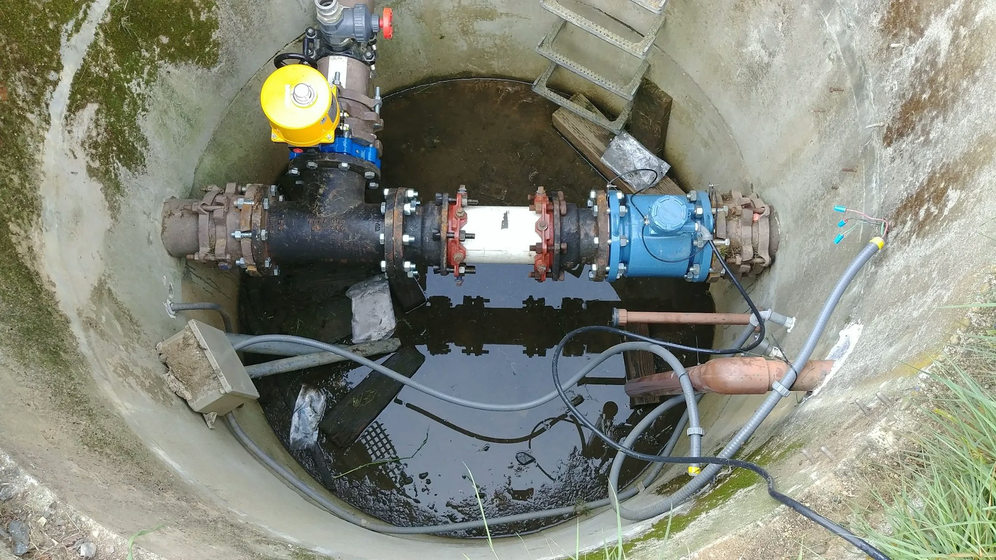 A water or sewage pump system with pipes and valves in a concrete well.