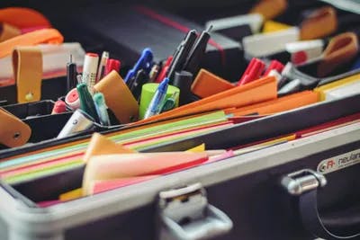 An organized case with colorful stationery: pens, markers, sticky notes, and paper clips.