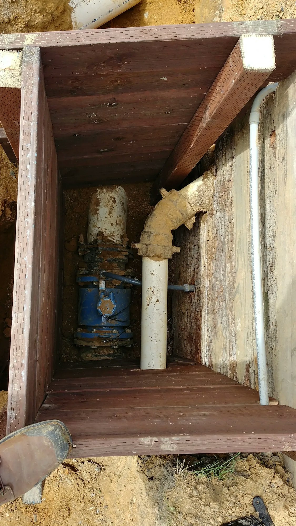 Underground water meter pit with pipes and valve, surrounded by wooden support structure.