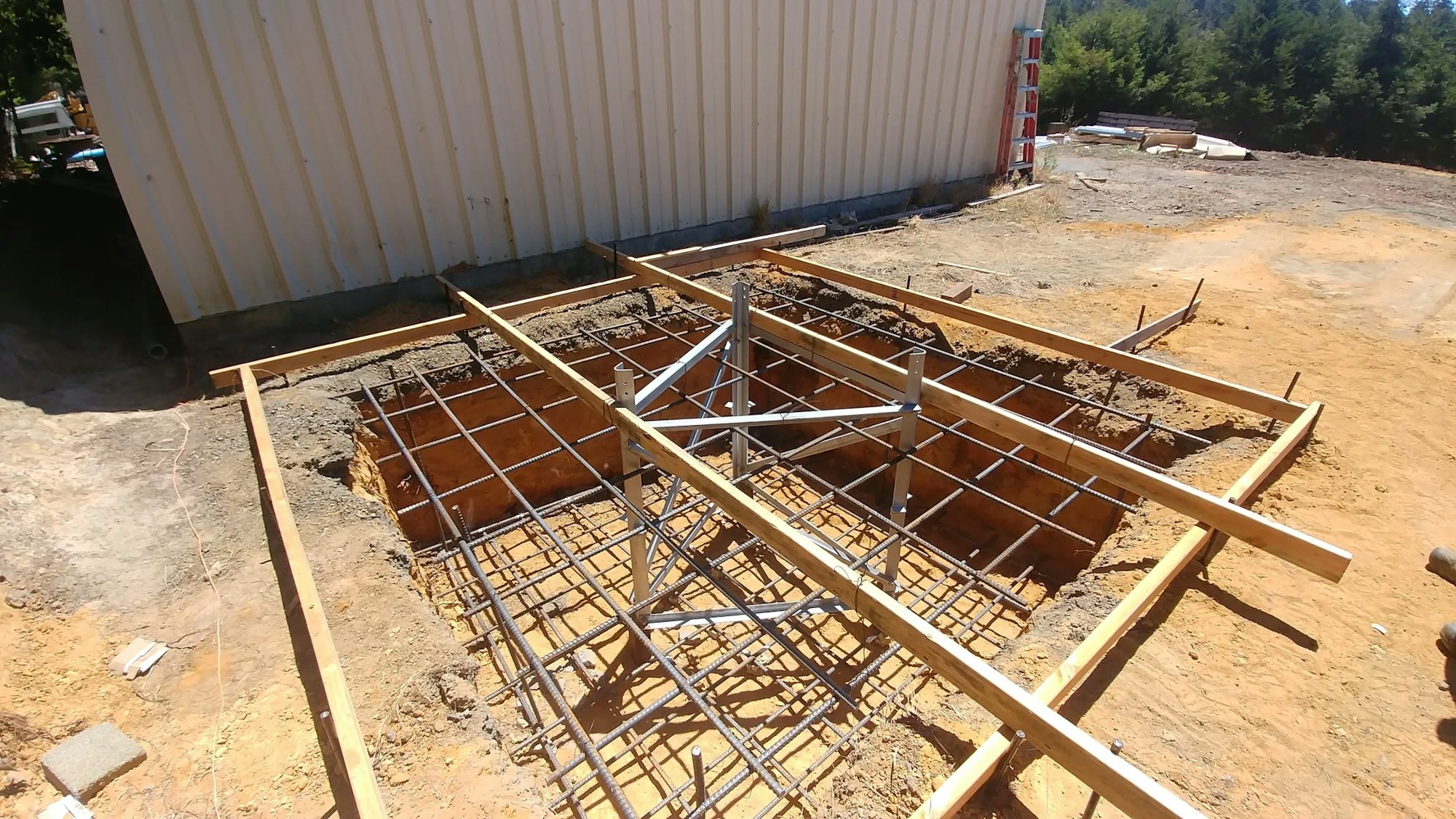 Construction site with excavated pits, rebar framework, and wooden forms for concrete foundation work.