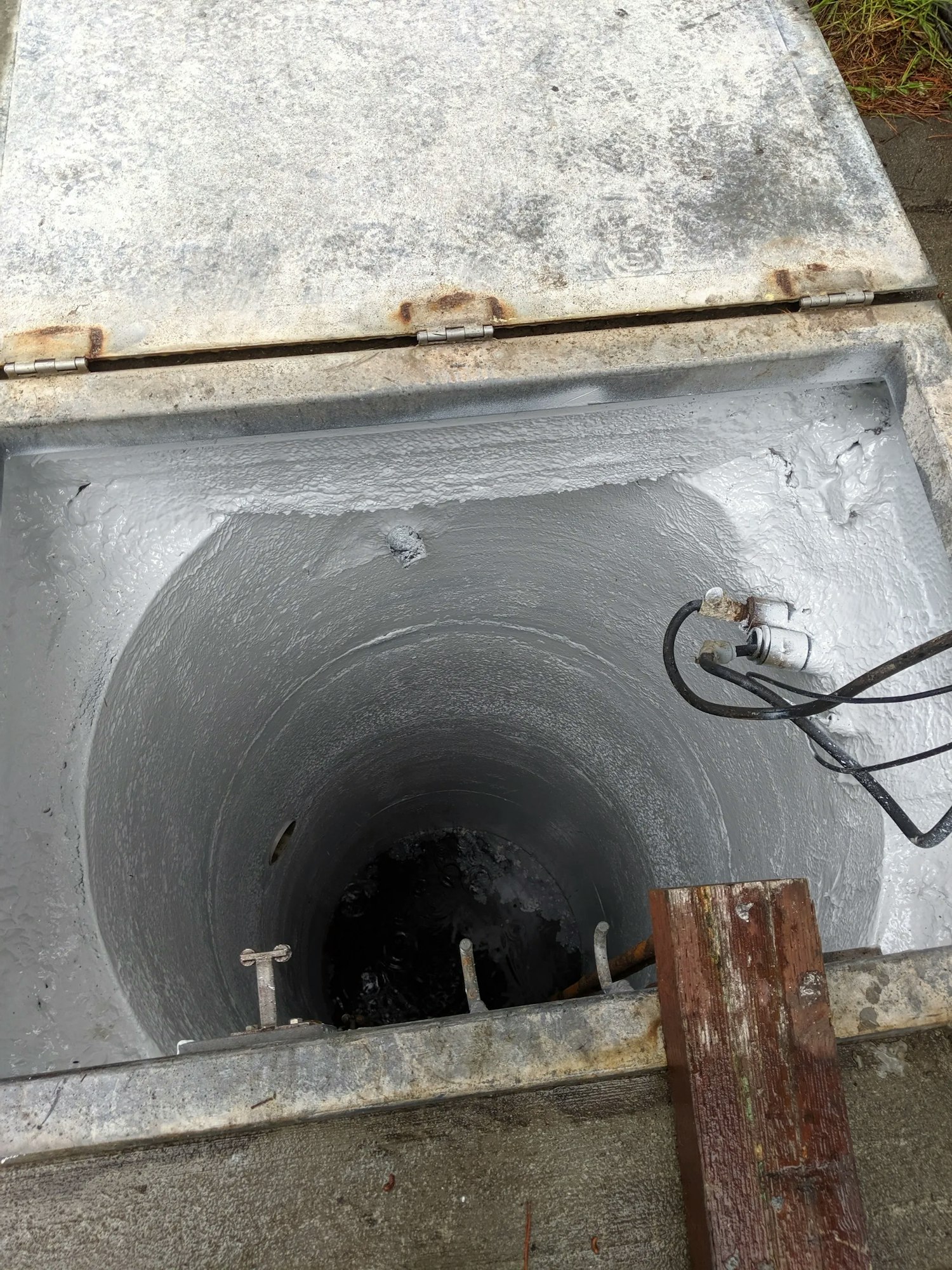 An open manhole cover with a view into a dark, wet shaft.