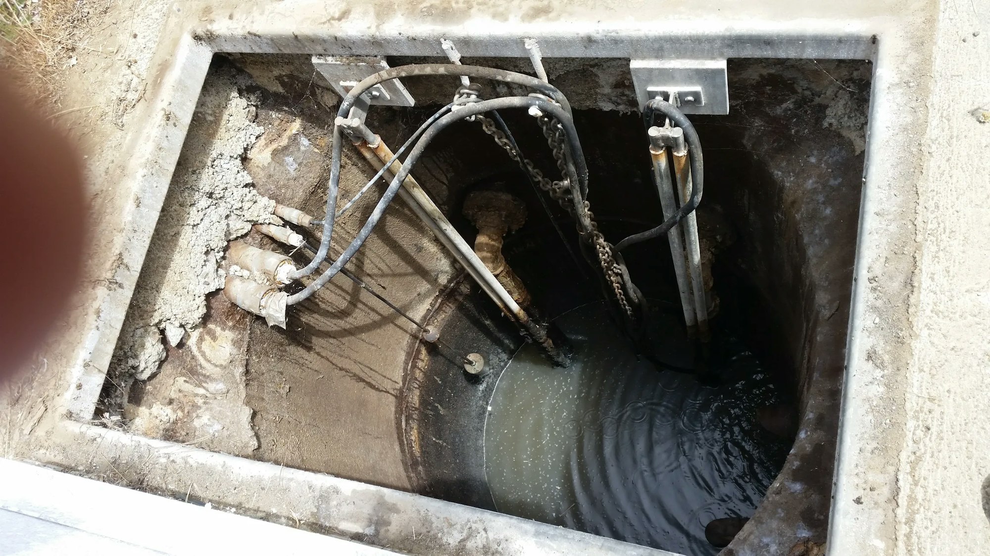 An open utility pit with cables, pipes, and a chain, possibly for maintenance purposes.