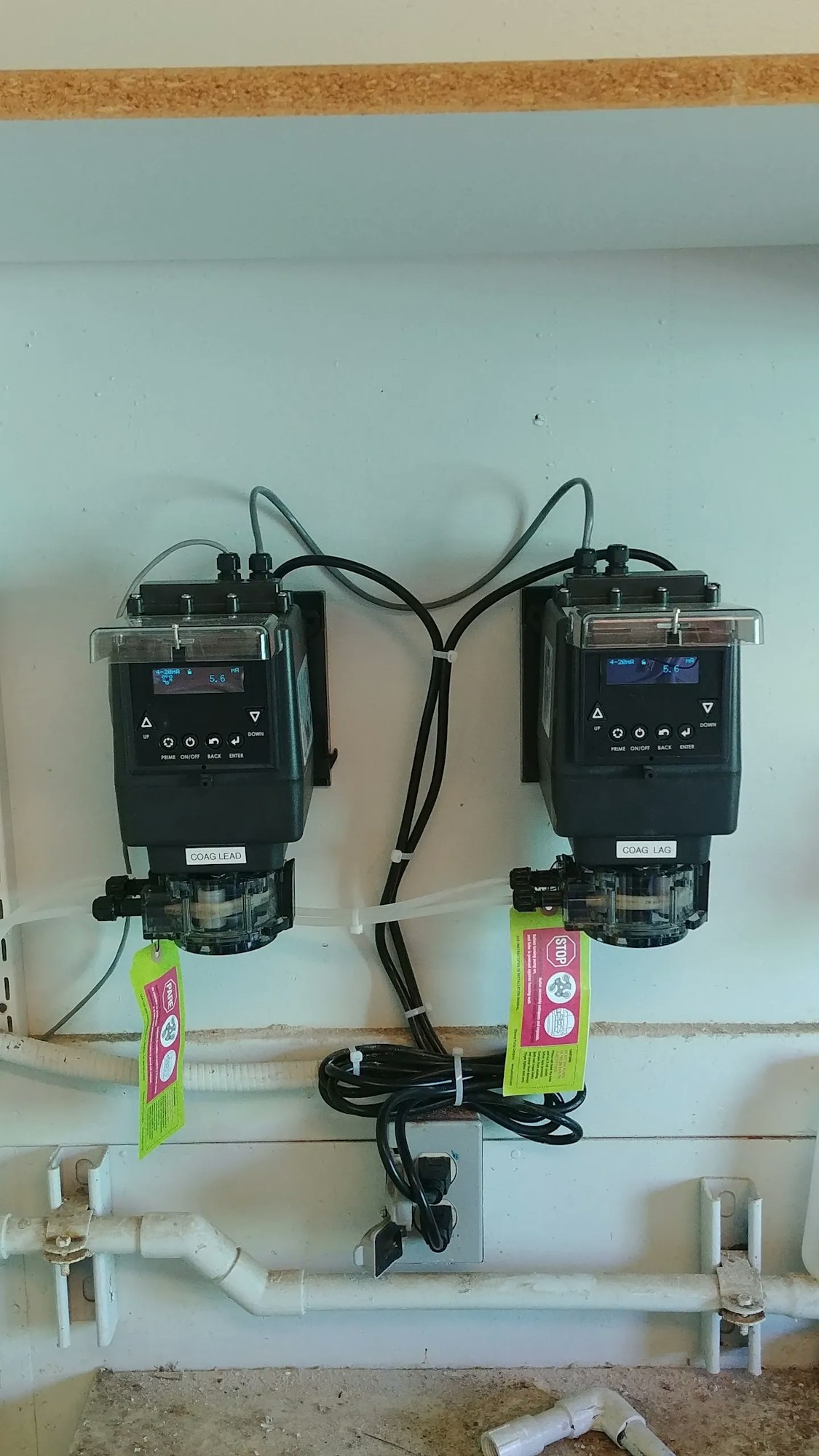 Two electronic water treatment devices mounted on a wall with wiring and plumbing.