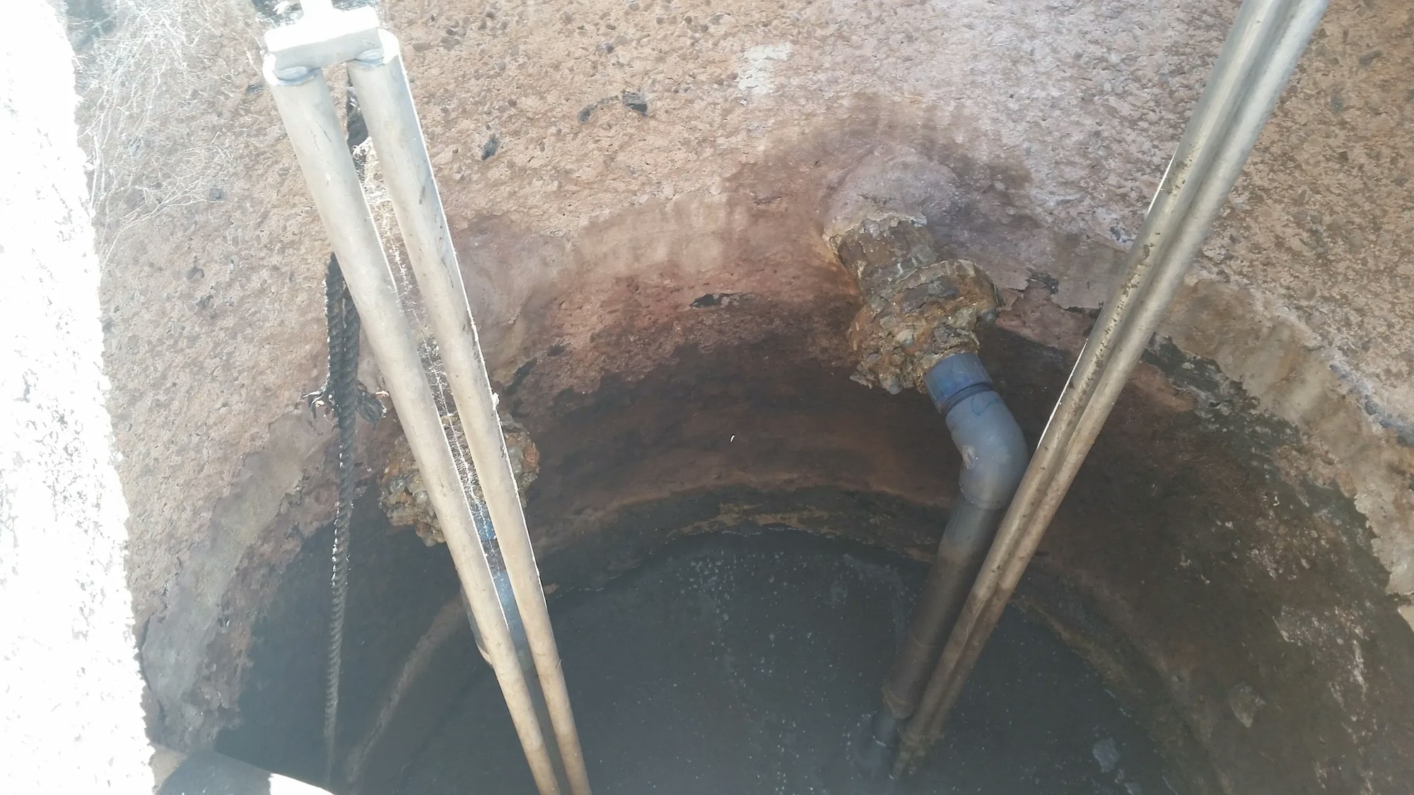 An open manhole with water at the bottom, pipes, and a ladder for access.