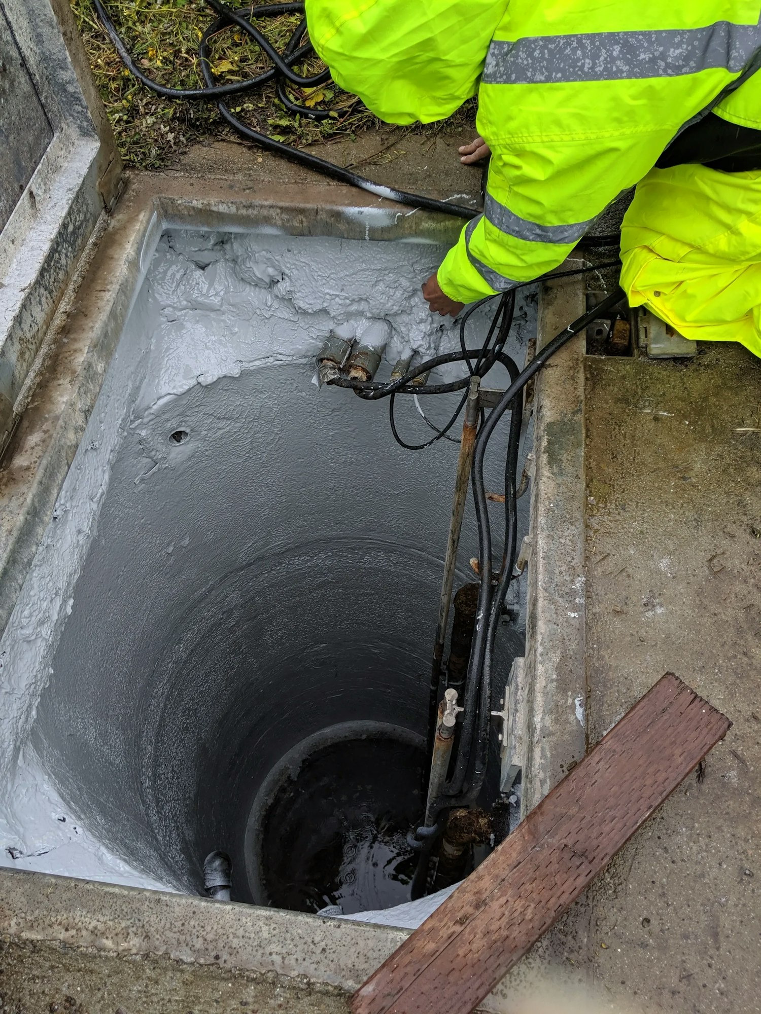 A worker in hi-vis gear standing by an open manhole with foam-filled interior and cables.