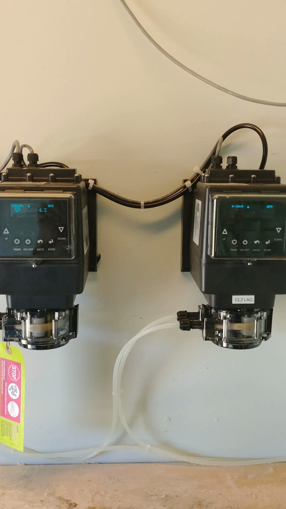 Two chemical dosing pumps with digital controls and tubing mounted on a wall.