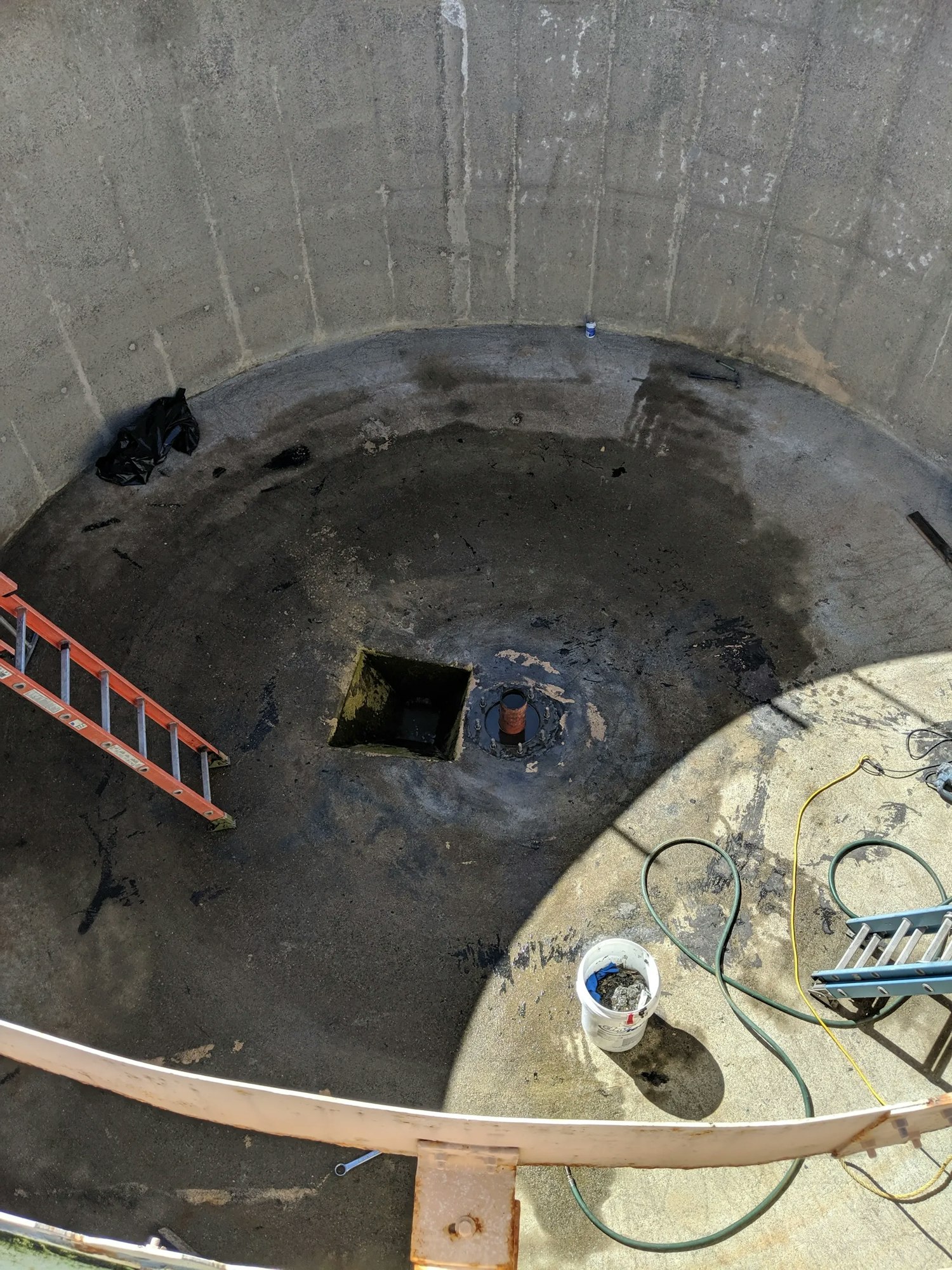Empty circular tank with ladder, hose, bucket, and small opening in the center.