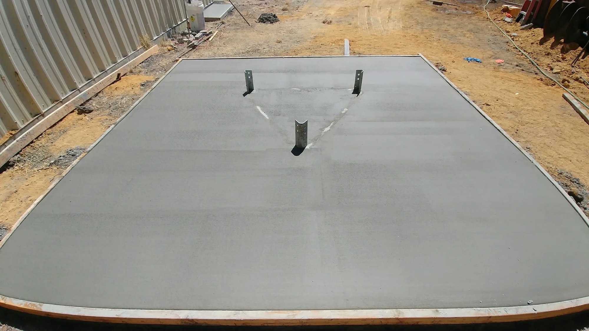 Freshly poured concrete slab with anchor bolts, construction site background.