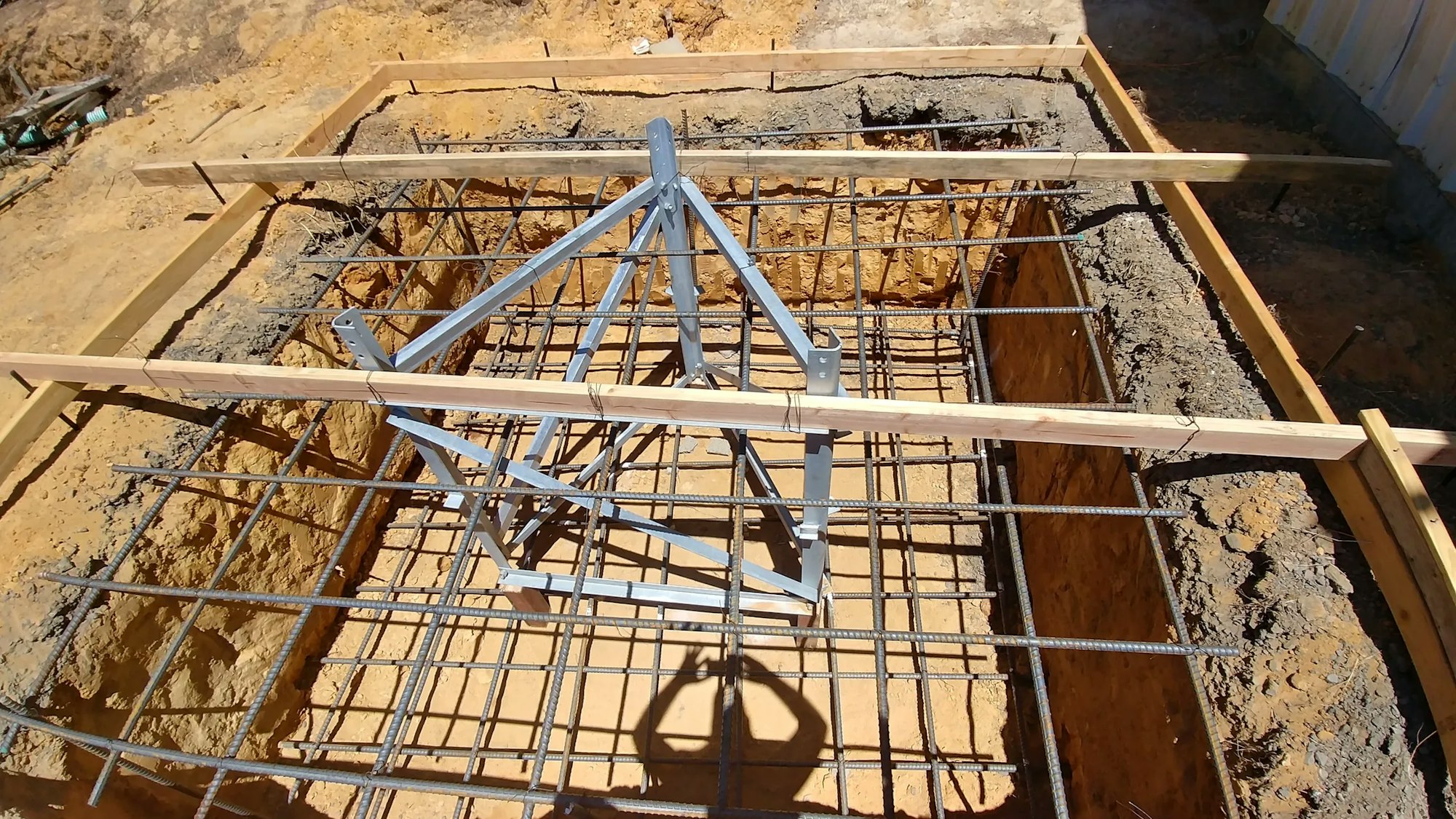 A construction site with wooden forms and reinforcing bars set for a concrete foundation, featuring a metal frame structure in the center.