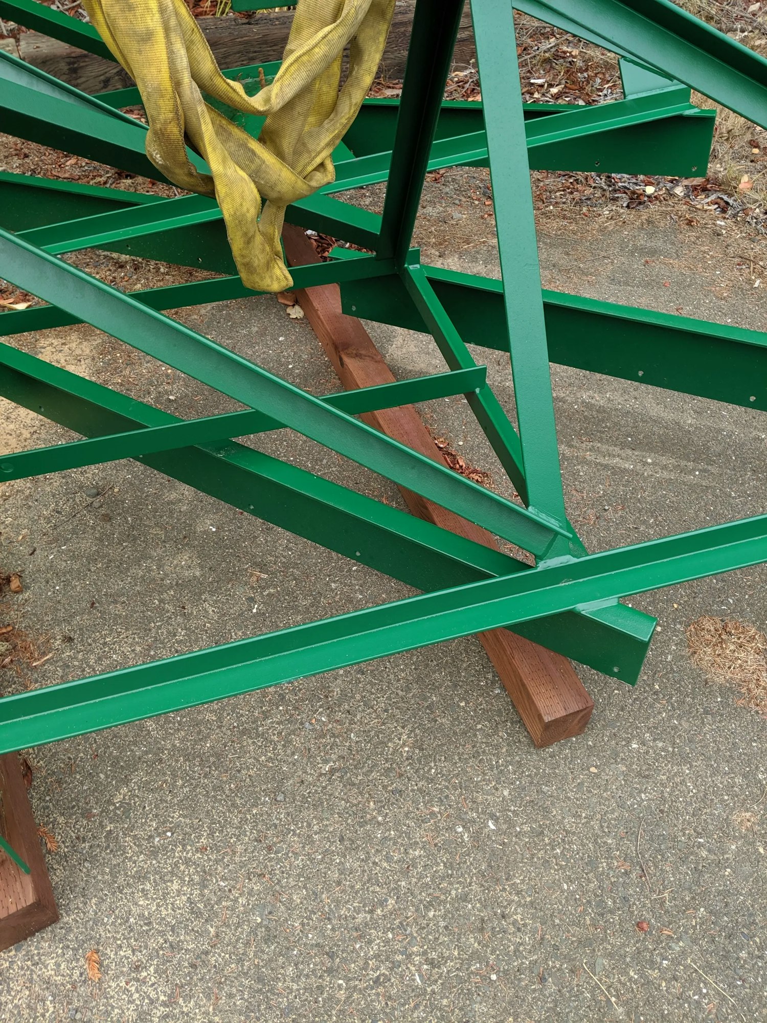 Green metal framework with wooden blocks and yellow straps on concrete.