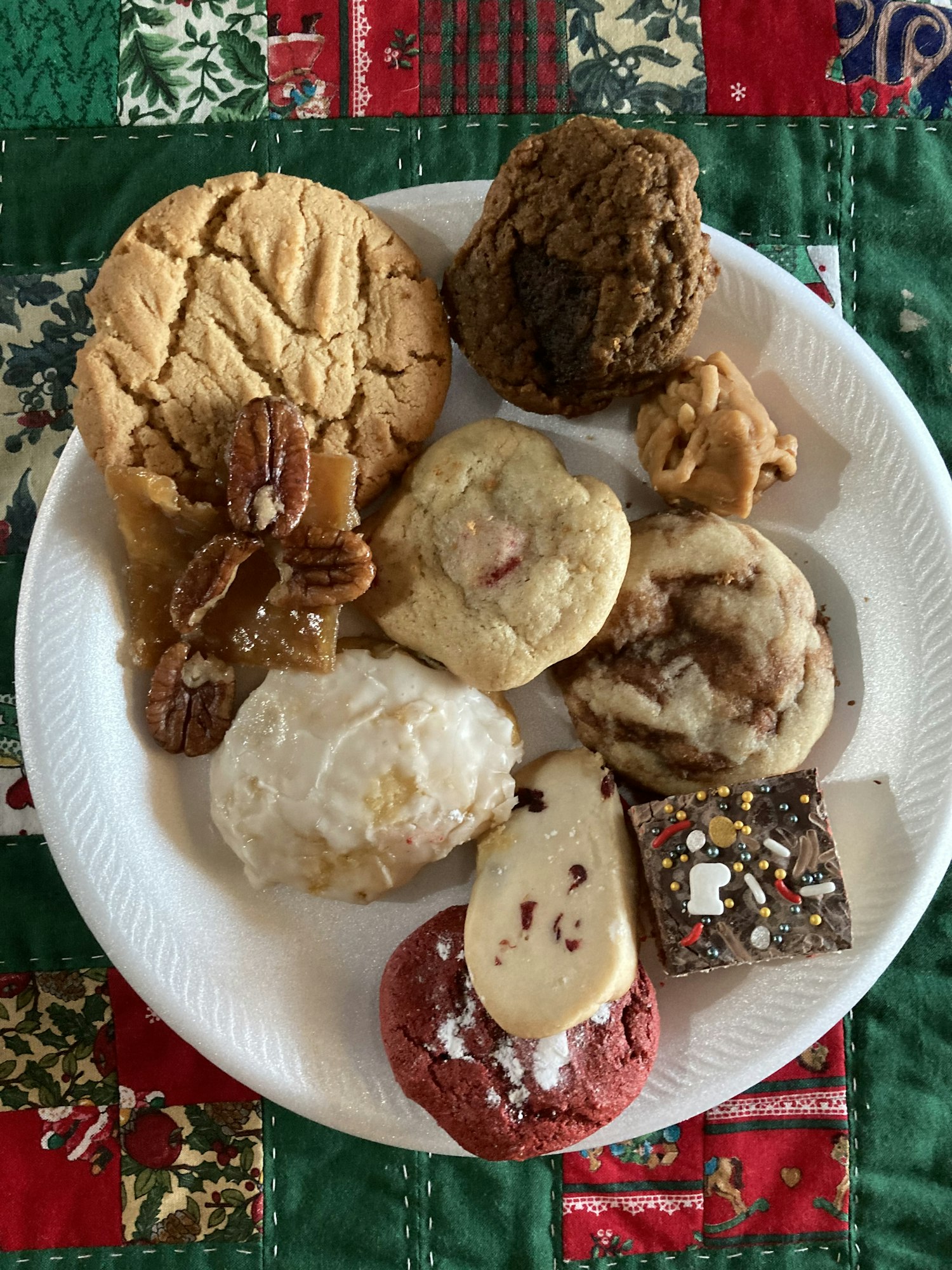 An assortment of cookies and sweets on a paper plate, placed on a festive quilted fabric.