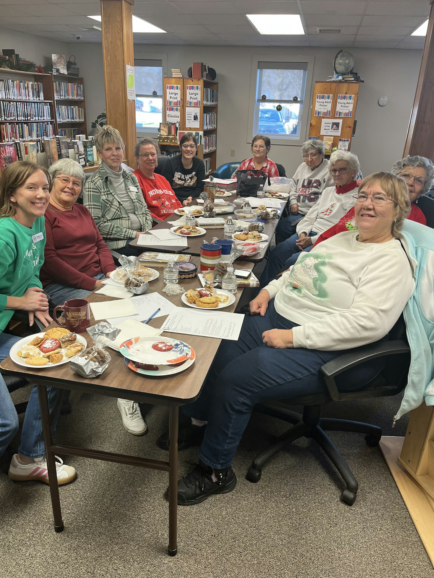 A group of people sitting around a table with plates of food in a library setting.