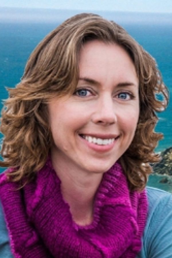 A person smiling in front of a scenic ocean background.